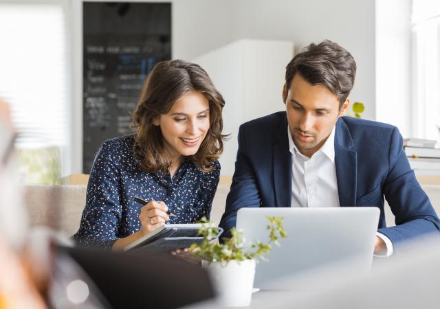 Deux professionnels de l'immobilier travaillent sur un dossier devant un ordinateur portable